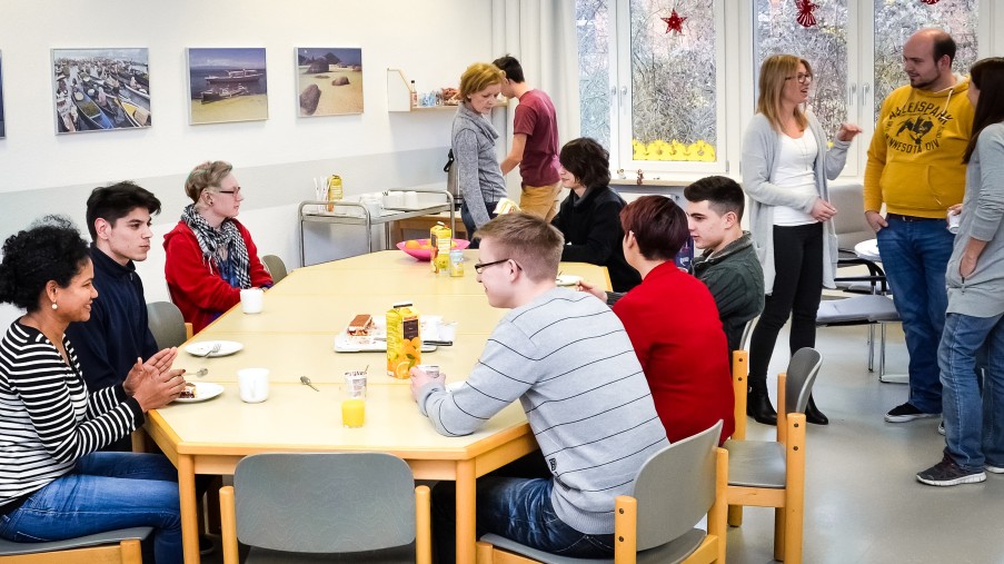 Viele Jugendliche im Gruppenraum, stehend und am Tisch sitzend.