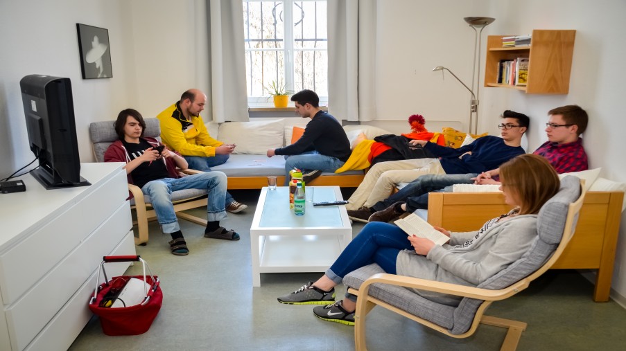 Jugendliche im Aufenthaltsraum, auf der Couch, Sessel, teils lesend, mit dem Smartphone spielend, Fernseh schauend.