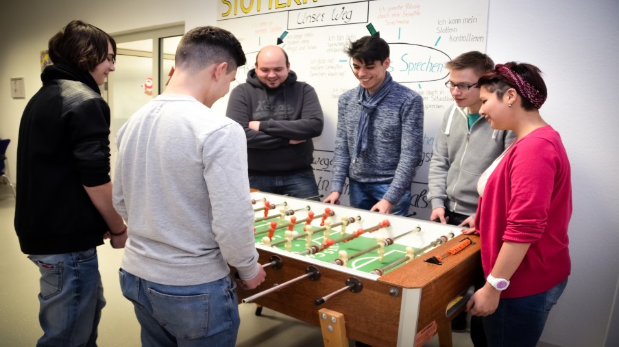 Jugendliche beim Kickerspielen auf Station mit Zuschauern.