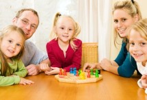 Eltern mit zwei Kindern beim Gesellschaftsspiel am Tisch sitzend.