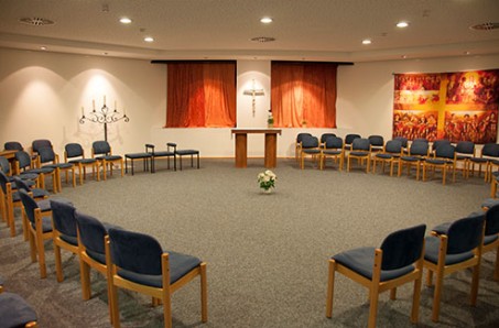 Blick in die Kapelle der LVR-Klinik Bonn, Stühle im Kreis gestellt, in der Mitte ein Blumenstrauß